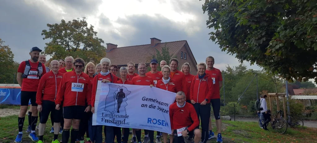 Gruppe von Läufern in roten Trikots mit Banner Gemeinsam an die Spitze vor herbstlicher Kulisse.
