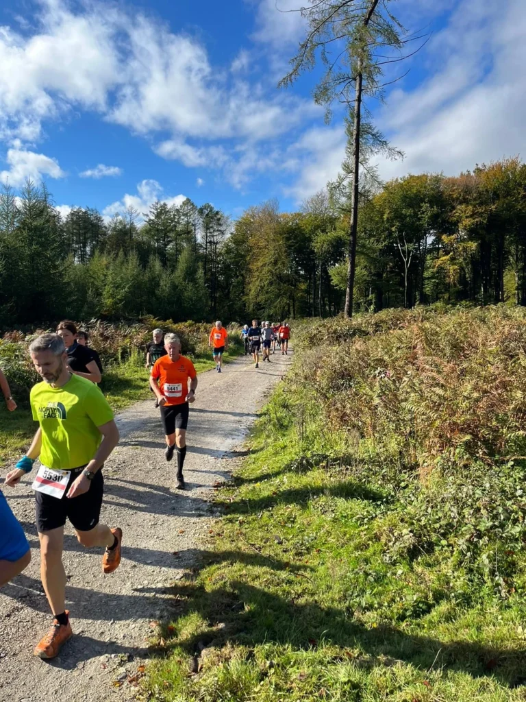 Läufer bei sonnigem Wetter auf Waldweg, Teilnehmer eines Laufwettbewerbs.