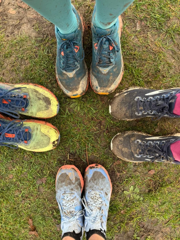Drei Personen stehen im Kreis, tragen schmutzige Laufschuhe auf Gras.