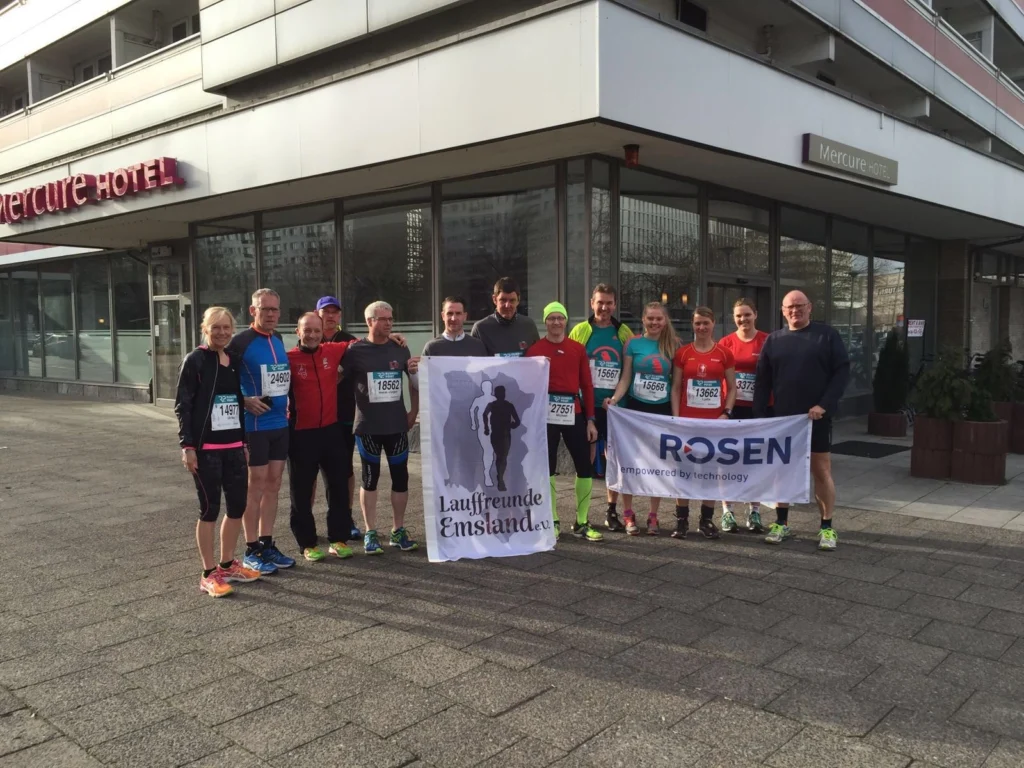 Läufergruppe posiert vor Mercure Hotel mit Bannern für Laufveranstaltung, 10 Personen in sportlicher Kleidung.