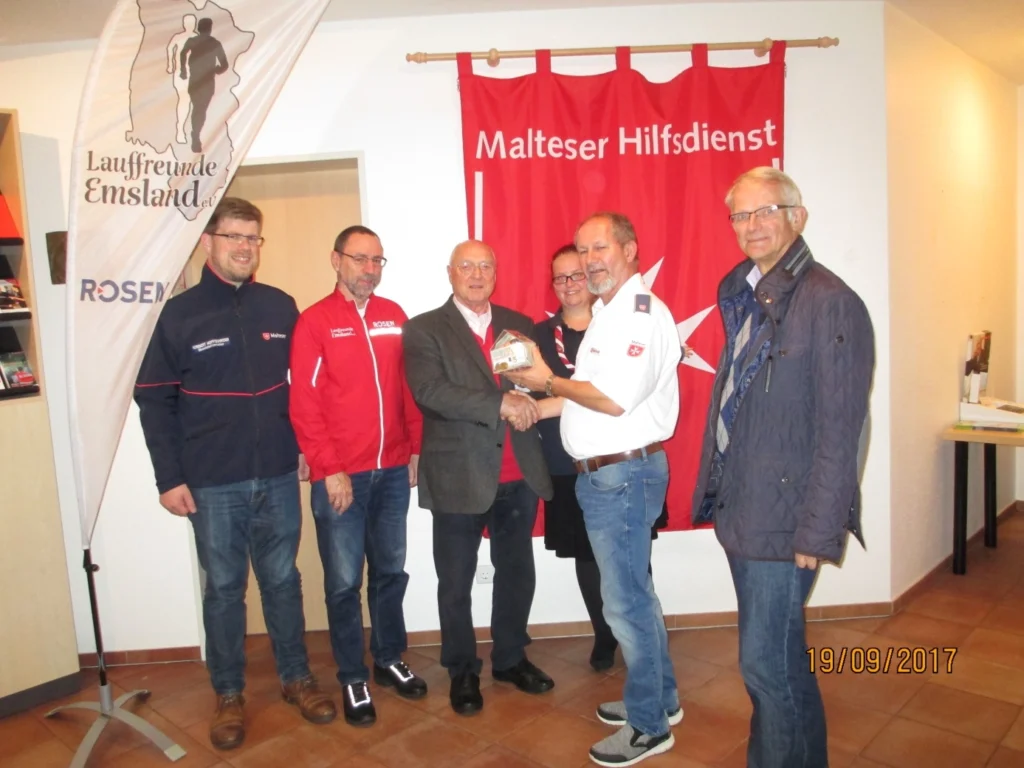 Gruppenfoto von Mitgliedern der Laufgruppe Emsland e.V. bei einer Veranstaltung mit dem Malteser Hilfsdienst, am 19. September 2017. Die Teilnehmer stehen vor einem Banner des Malteser Hilfsdienstes und zeigen eine Auszeichnung.