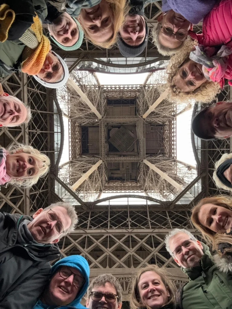 Gruppe von Menschen, die unter dem Eiffelturm in Paris stehen, Blick nach oben auf die beeindruckende Stahlkonstruktion.