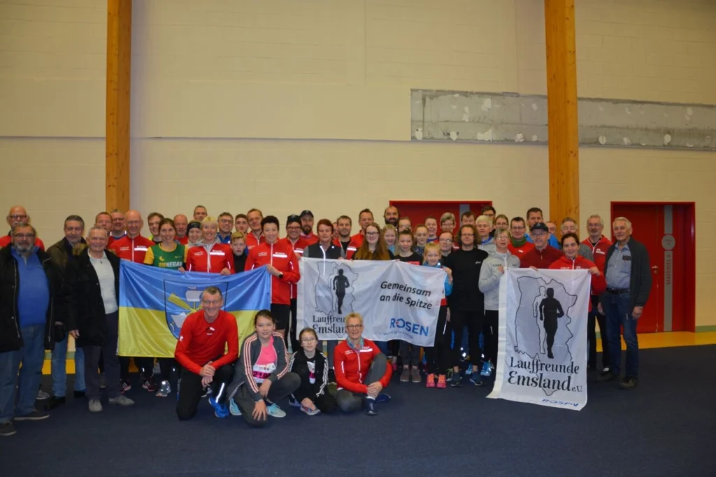 Gruppenfoto der Laufgemeinschaft "Lauffreunde Emsland" mit Mitgliedern in roten Trikots, die Fahnen halten. Die Veranstaltung fördert den Gemeinschaftssport und zeigt die Vielfalt der Teilnehmer in einem sportlichen Umfeld.