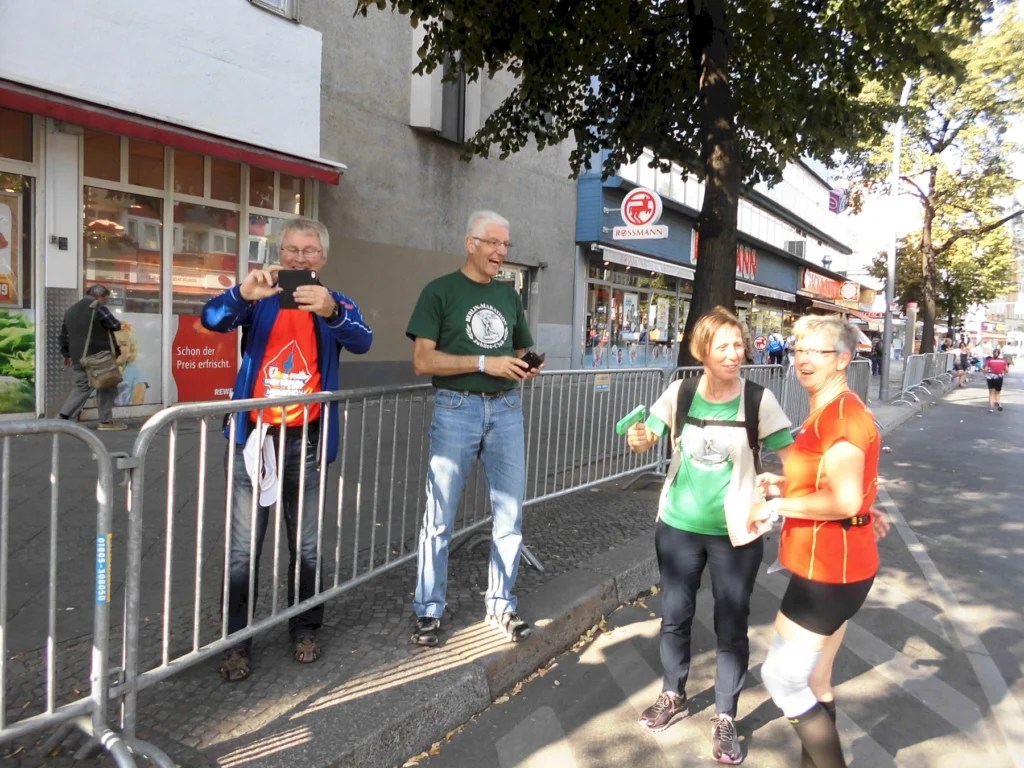 Gruppe von Menschen macht Fotos und feuert Läufer bei einem Marathon in einer städtischen Einkaufsstraße an.