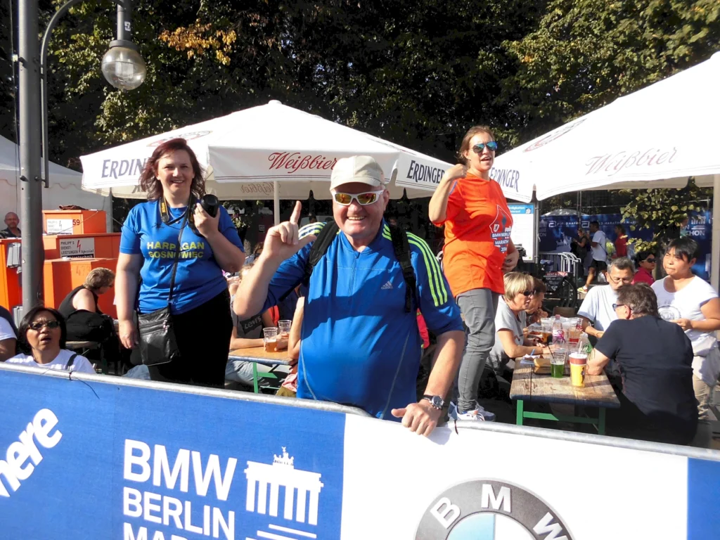 Gruppe von Menschen beim Berlin Marathon, fröhlich in der Zuschauermenge, mit Sonnenschirmen im Hintergrund.