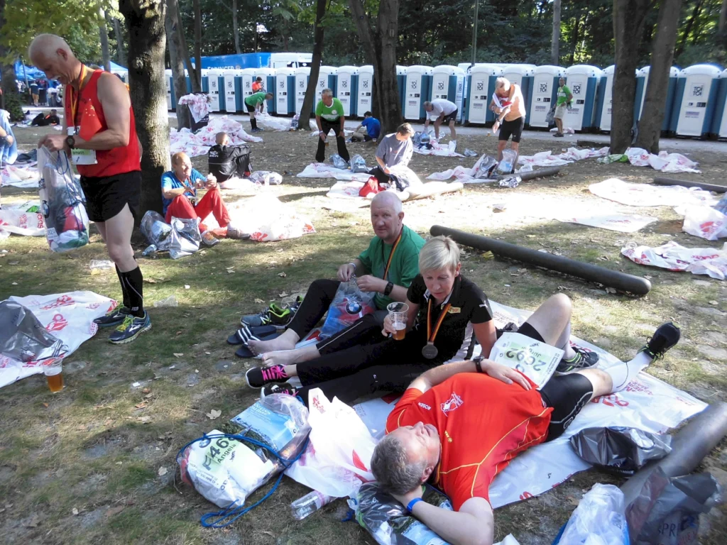 Teilnehmer eines Marathons entspannen auf dem Boden im Park nach dem Lauf, umgeben von Taschen und Erfrischungen.