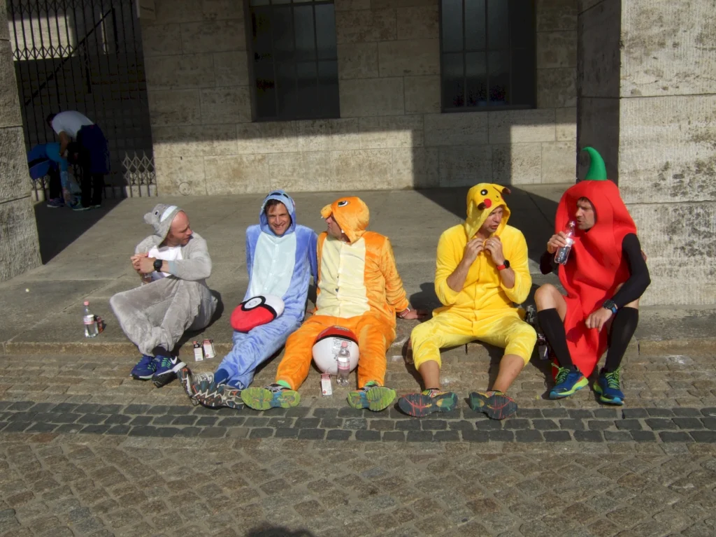 Fünf Personen in Tier- und Gemüse-Kostümen sitzen auf dem Boden und trinken Wasser bei einer Pause.