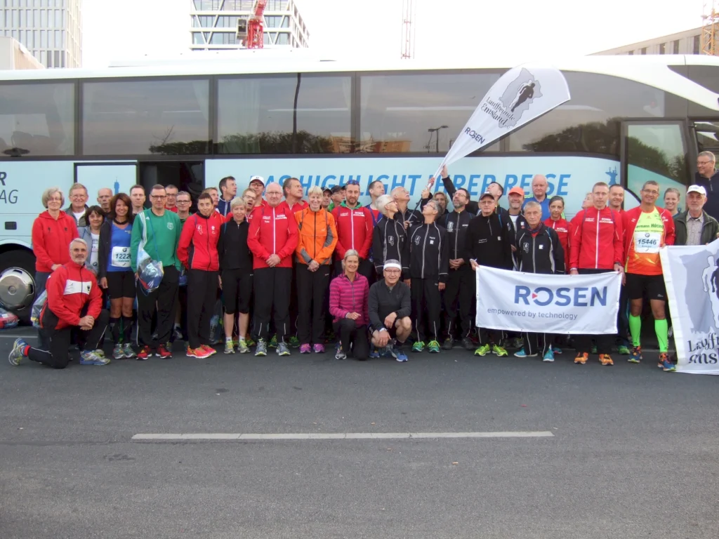 Gruppe von Läufern in Sportkleidung posiert mit Bannern vor einem Reisebus für ein Teamfoto bei einem Sportevent.