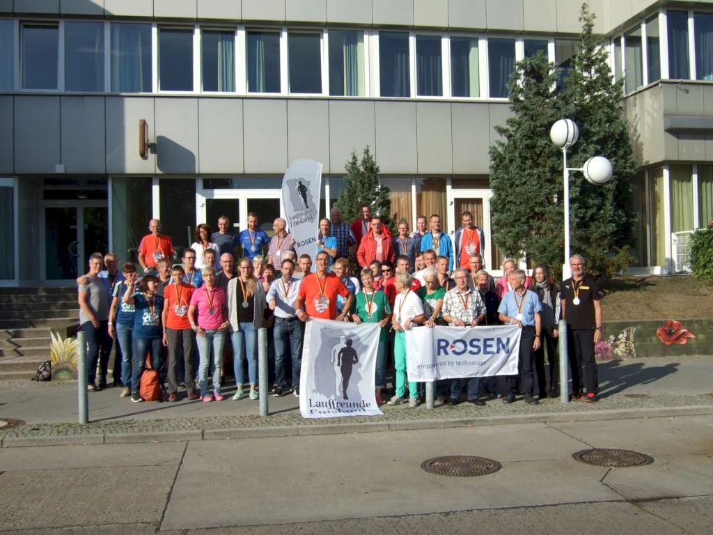 Gruppe von Läufern mit Medaillen posiert vor einem Gebäude, hält Banner mit „Lauffreunde“ und „ROSEN“.
