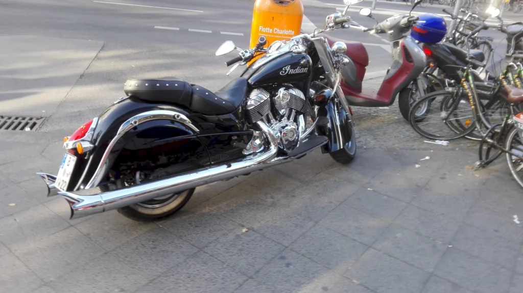 Schwarzes Motorrad und Motorroller parken auf urbanem Gehweg neben Fahrrädern.