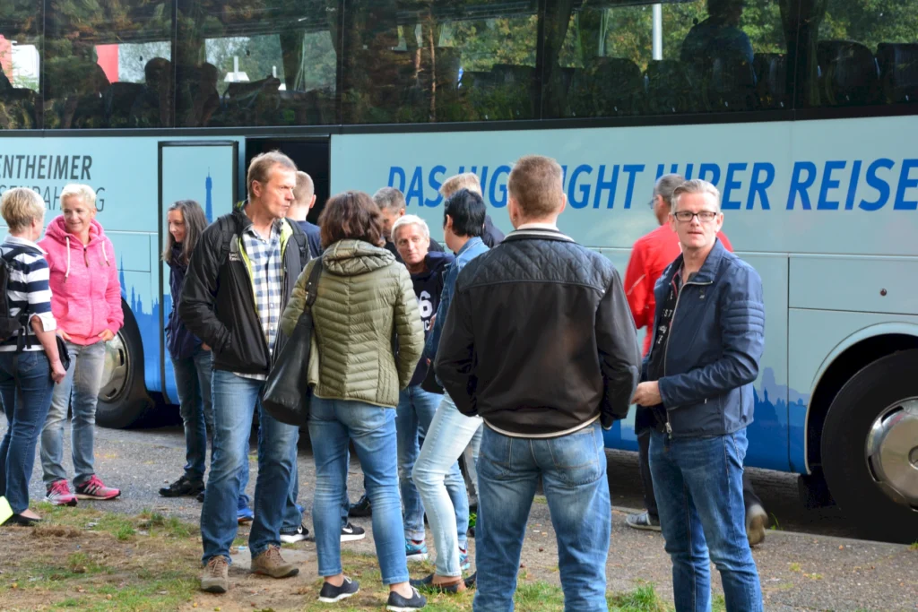 Gruppe von Menschen steht vor einem Reisebus auf einem Rastplatz, Plausch vor Weiterfahrt.