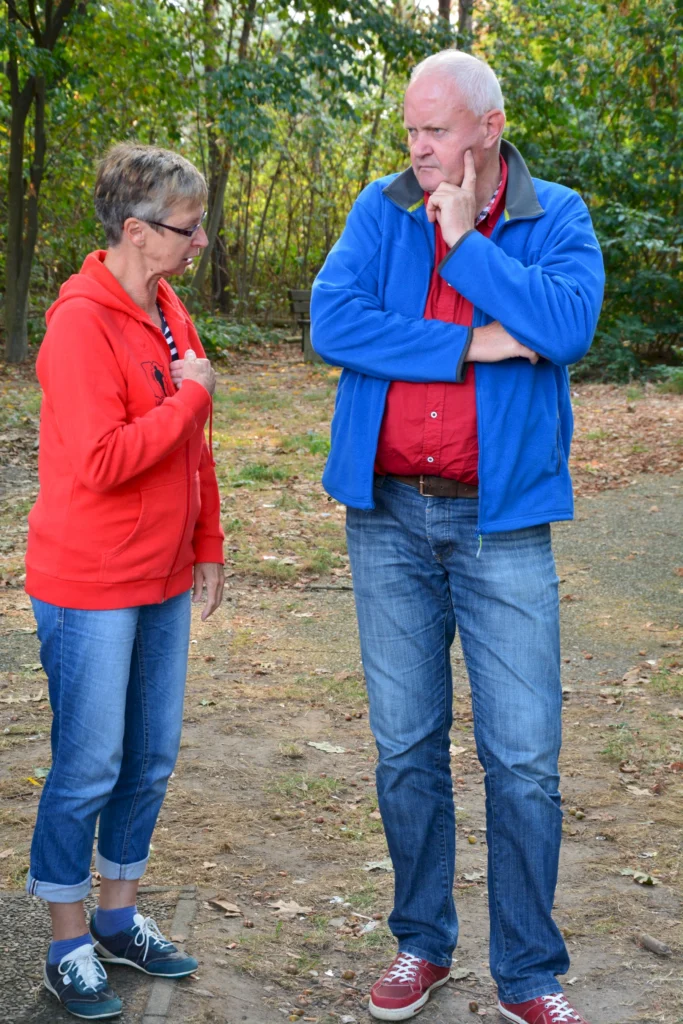 Zwei Personen unterhalten sich draußen im Wald bei Herbstwetter, beide tragen bunte Freizeitkleidung.