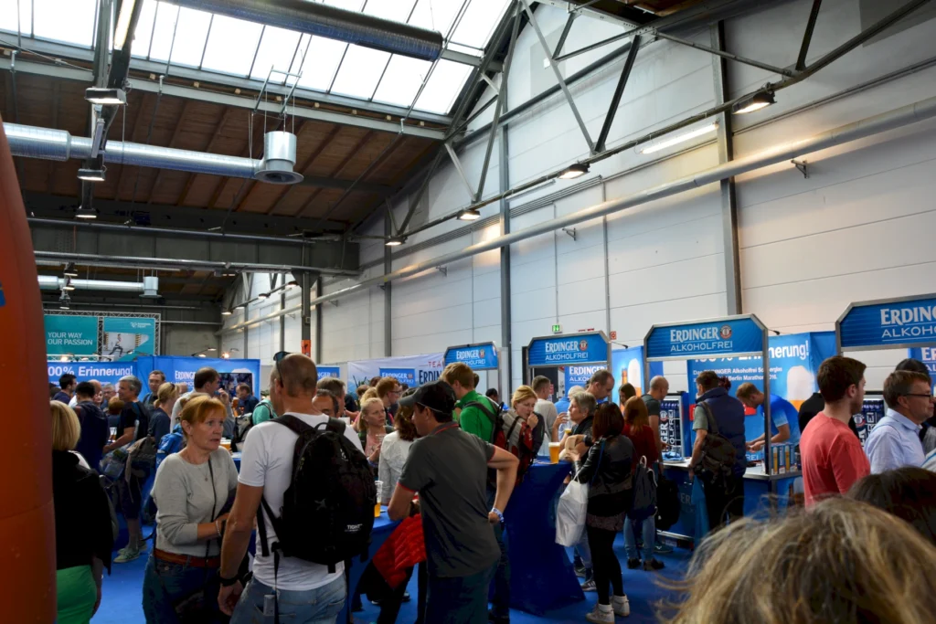 Menschenmenge auf Messe mit Erdinger Alkoholfrei-Stand. Viele Besucher interagieren und probieren Getränke.