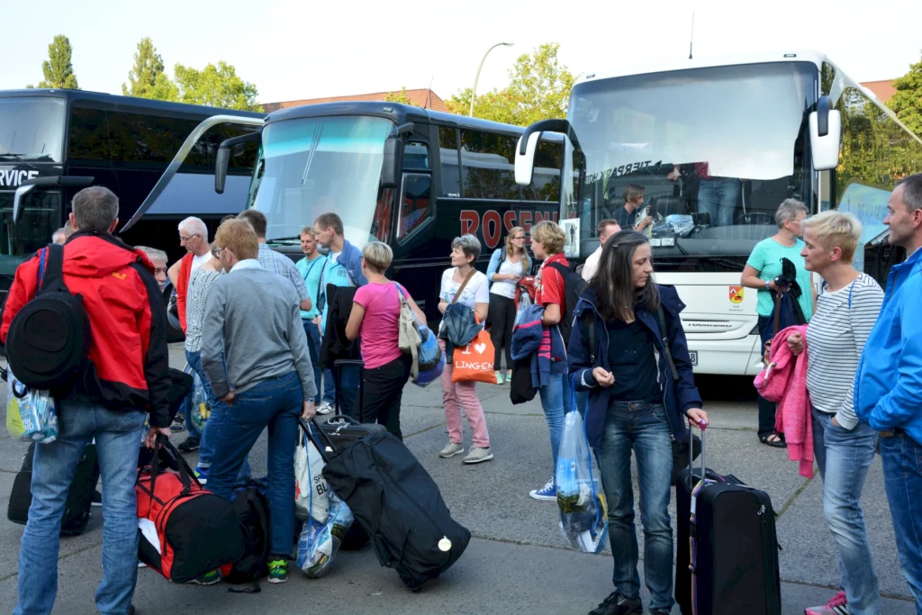 Reisegruppe wartet mit Gepäck vor mehreren Reisebussen, bereitet sich auf Abfahrt vor.