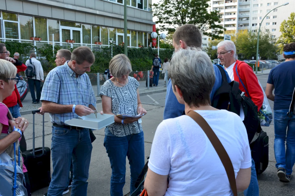 Menschen stehen in einer Warteschlange vor einem Gebäude und füllen Formulare aus.