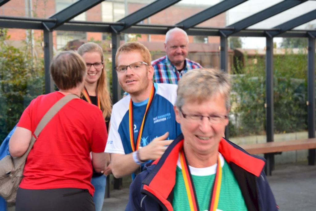 Gruppe von Menschen bei einem Event, lachend und Medaillen tragend, stehen in einem überdachten Außenbereich.