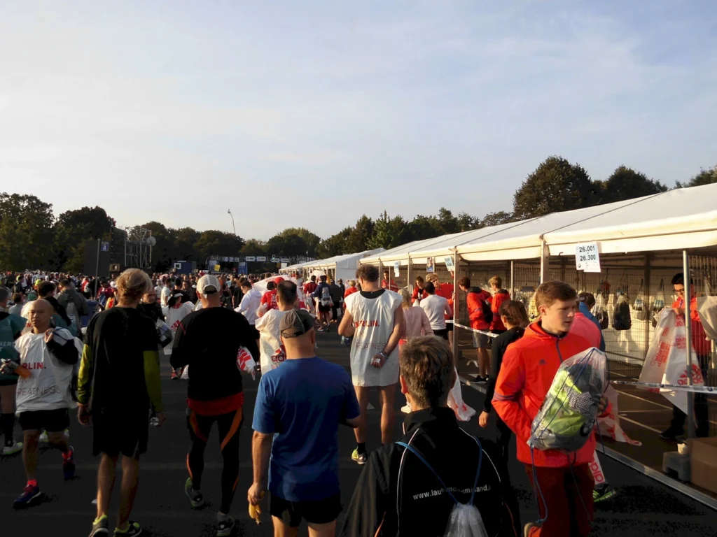 Teilnehmer eines Marathon-Events bewegen sich durch ein Areal mit Zeltständen, wo sie ihre Startnummern abholen. Die Veranstaltung zieht zahlreiche Läufer an, die sich auf den Wettkampf vorbereiten.