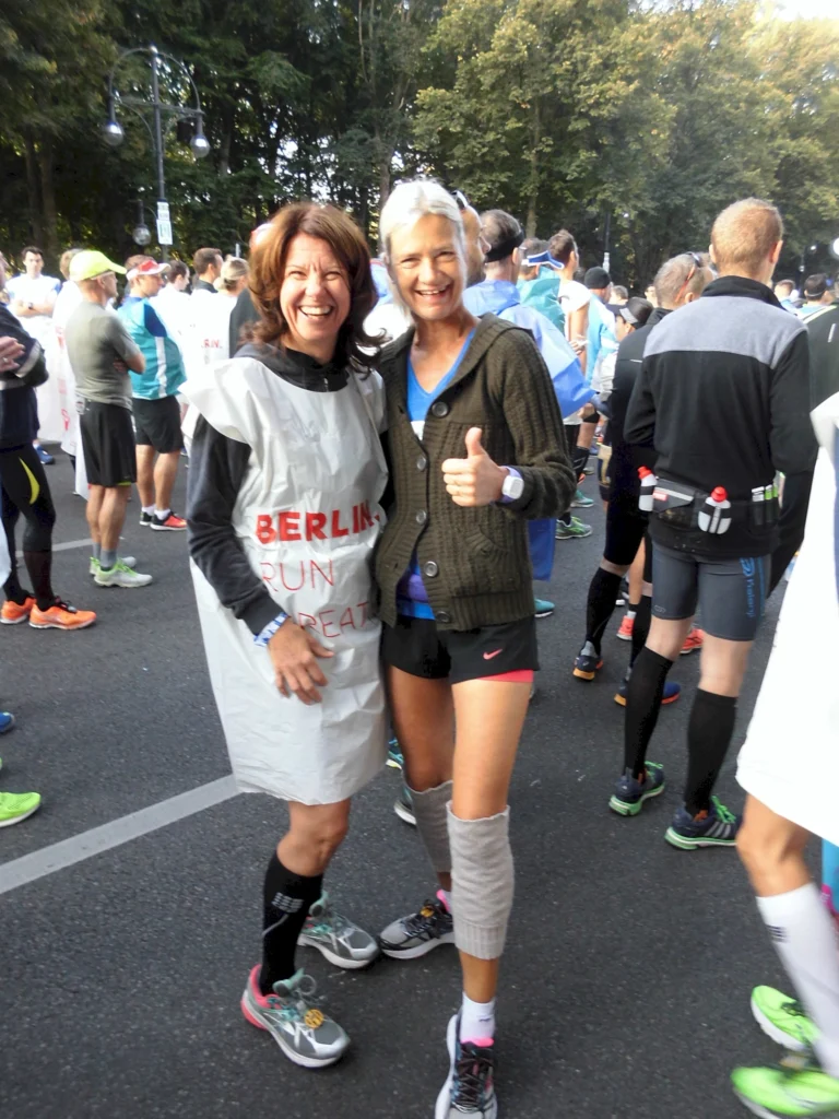 Läuferinnen beim Berlin-Marathon, die fröhlich in Sportkleidung posieren, umgeben von anderen Teilnehmern.