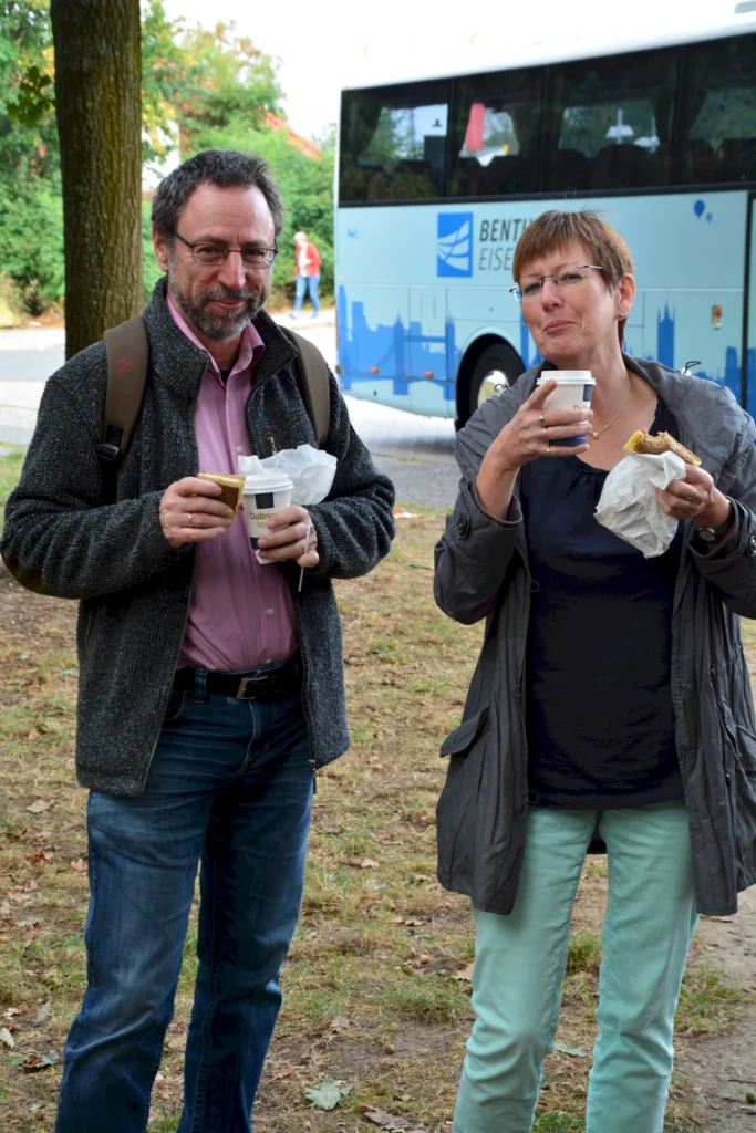 Zwei Personen genießen Kaffee und Snacks vor einem Reisebus im Freien.