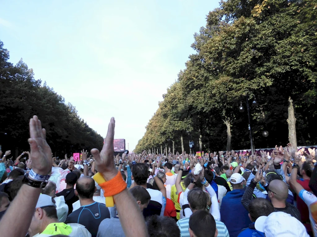 Teilnehmer eines Marathons stehen jubelnd auf einer baumgesäumten Straße, Hände in der Luft, bei klarem Himmel.