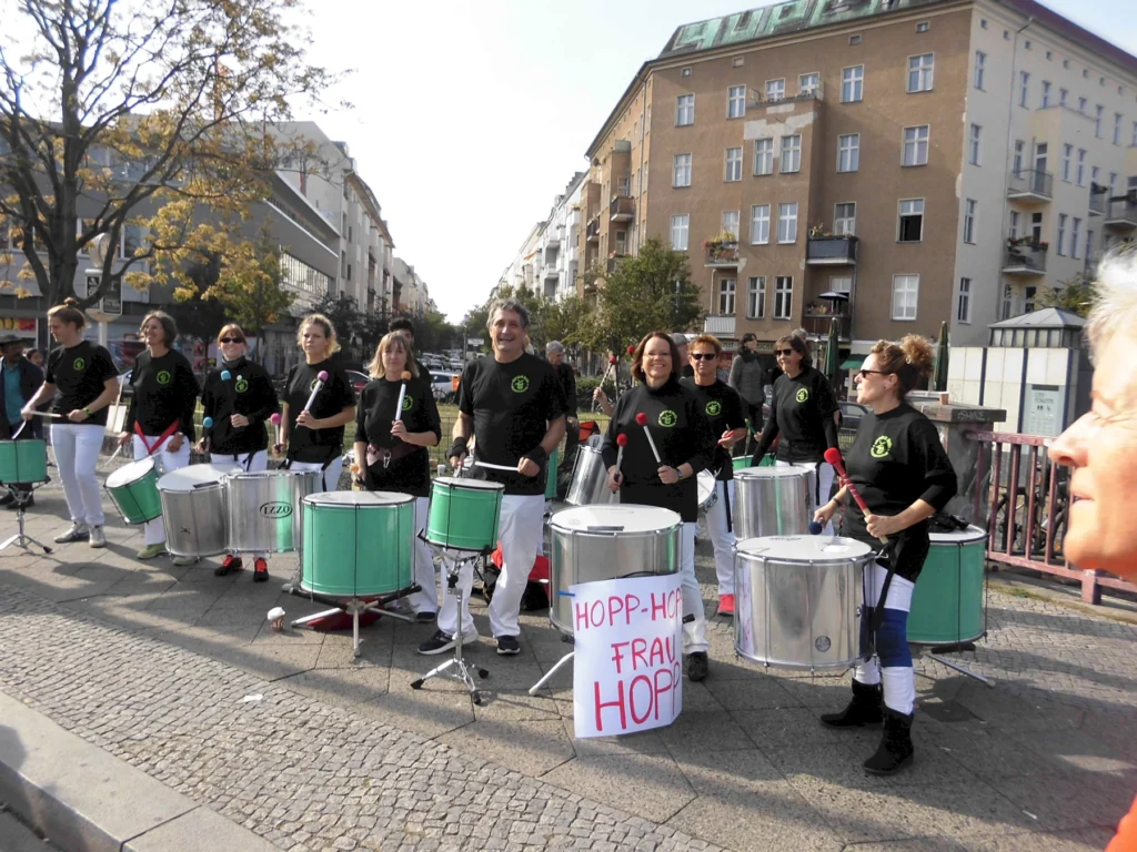 Musikgruppe mit Trommlern spielt im Freien bei sonnigem Wetter auf einer gepflasterten Straße in der Stadt.