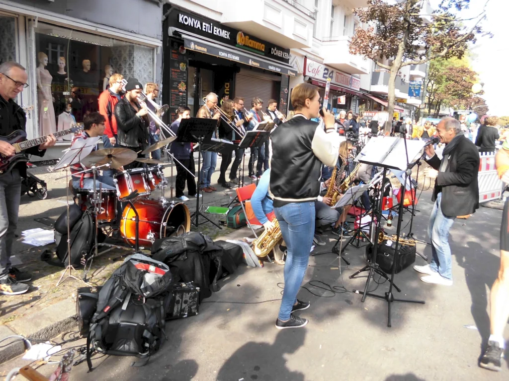 Straßenmusikerband spielt live auf einem Bürgersteig, umgeben von einer Menschenmenge und Geschäften.