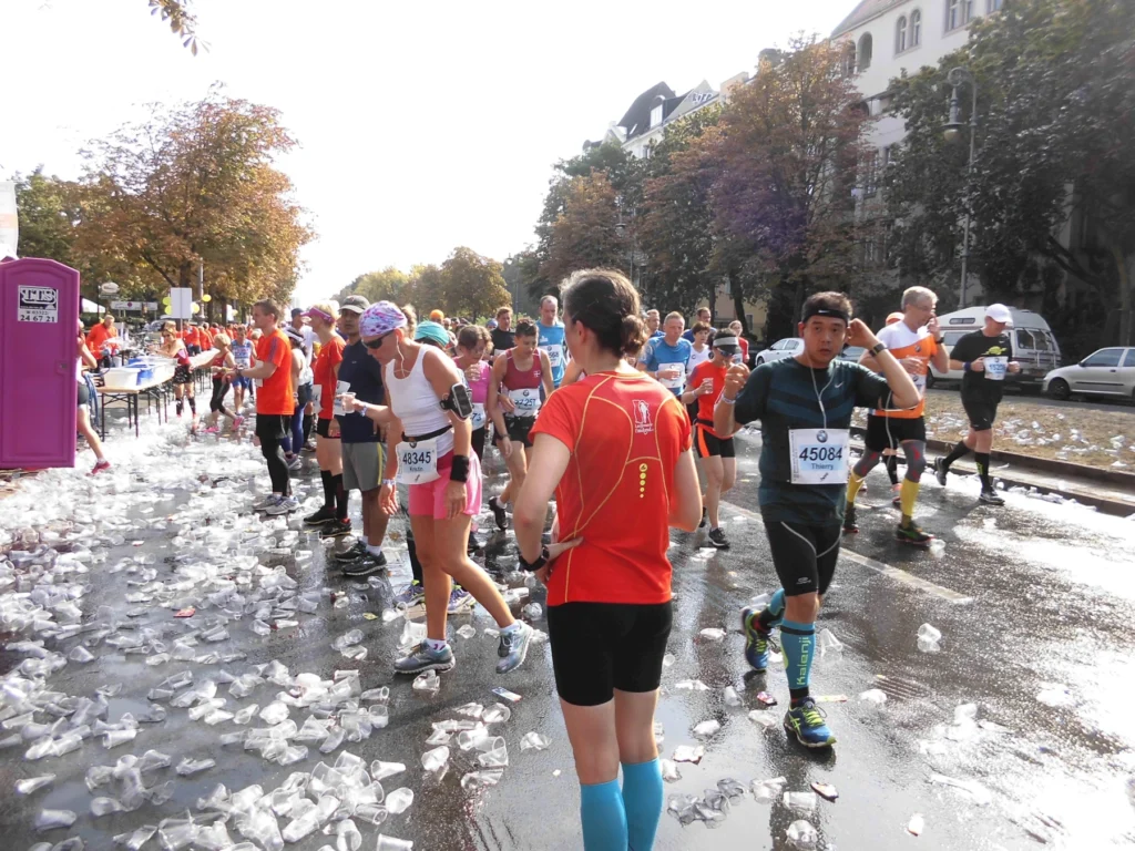 Läufer erfrischen sich bei einem Marathon, passieren eine Wasserstation mit Bechern auf der Straße bei sonnigem Wetter.