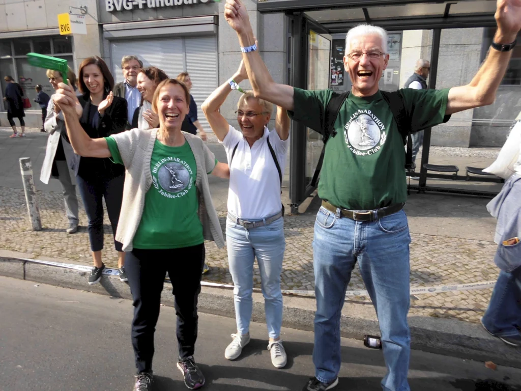 Menschen jubeln fröhlich bei einer Straßenveranstaltung in Berlin, tragen Marathon-T-Shirts, lächelnd in die Kamera.