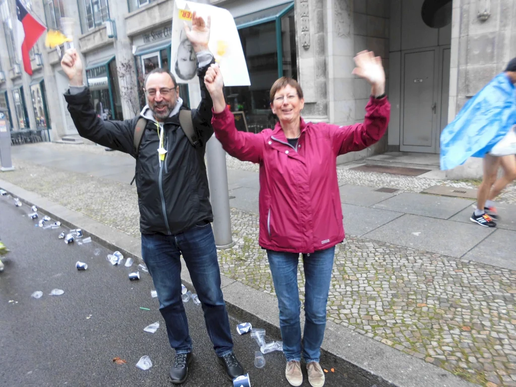 Zwei Personen jubeln auf Straße mit leeren Bechern um sie herum, fröhliche Stimmung bei einer Veranstaltung im Freien.