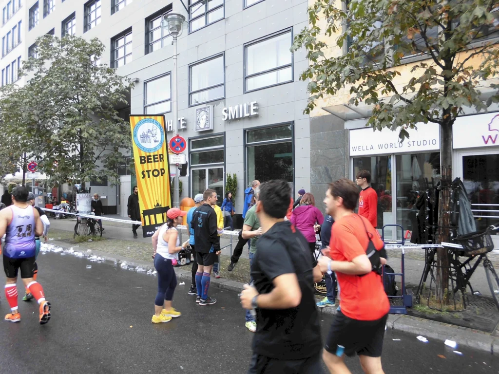 Läufer beim Marathon, passieren einen Beer Stop in der Stadt, umgeben von Gebäuden und Zuschauern entlang der Strecke.
