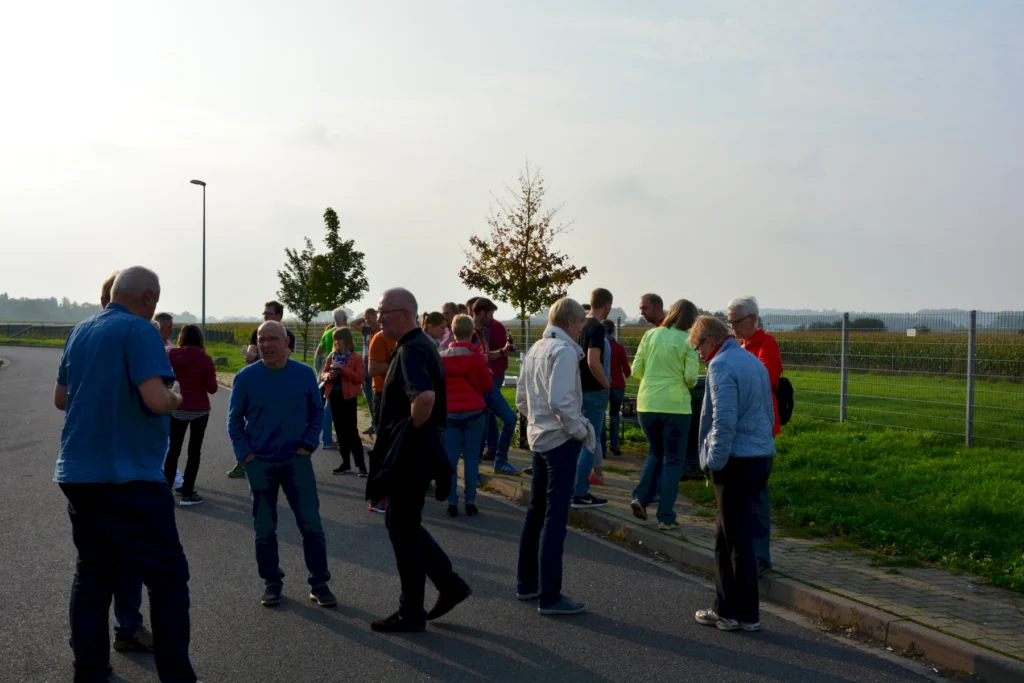 Gruppe von Menschen unterhält sich im Freien auf einer Straße neben einem Feld an einem sonnigen Tag.