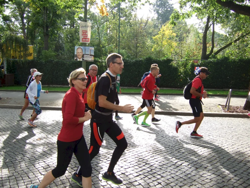 Läufergruppe beim Marathonlauf im Grünen, sonniger Tag, ambitioniertes Rennen, diverse Teilnehmer in Sportbekleidung.