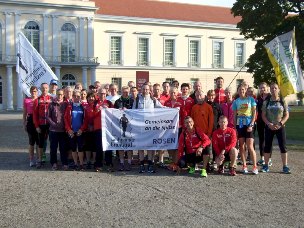 Gruppe von Läufern vor historischem Gebäude, hält Banner mit Teamnamen und Motto, vereint für Laufevent.