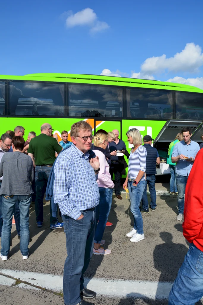 Gruppe von Menschen steht vor einem grünen Reisebus bei sonnigem Wetter.