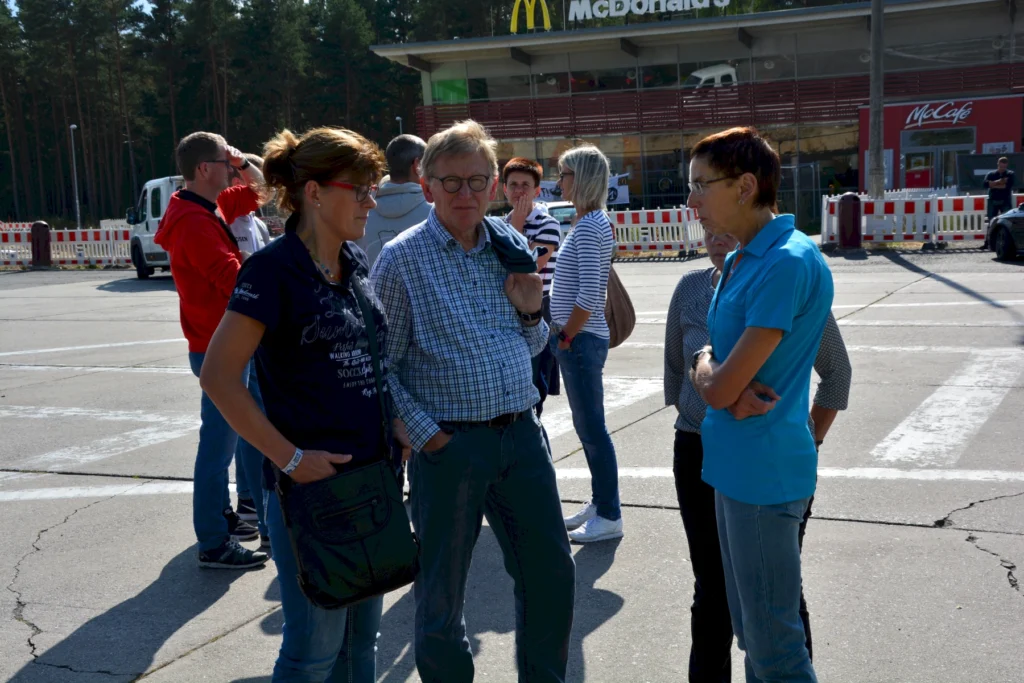 Gruppe von Menschen vor einem McDonald's bei sonnigem Wetter, im Gespräch auf einem Parkplatz.