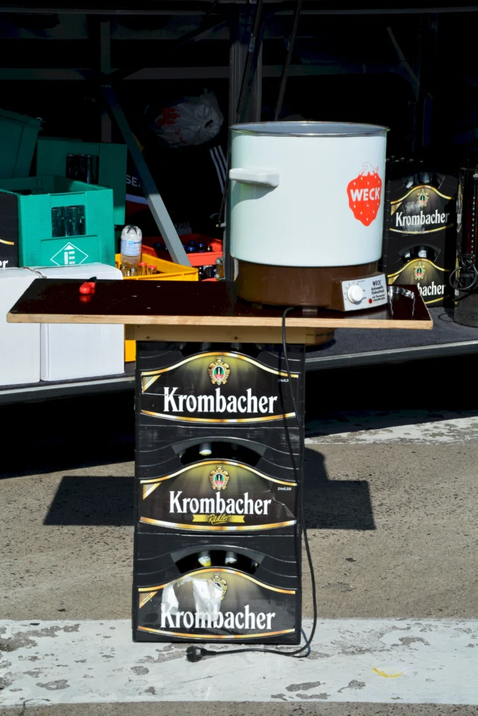 Selbstgebauter Biertisch aus Krombacher-Kisten mit elektrischem Einkochtopf von Weck auf einem Straßenmarkt.