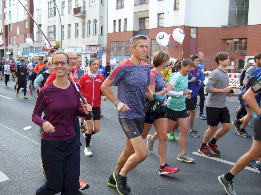 Menschen laufen bei Straßenlauf-Event in Stadtumgebung, fröhliche Atmosphäre, bunte Sportkleidung und Ballons.