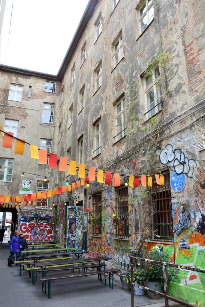 Bunte Graffiti und Papierfahnen in einem Berliner Innenhof mit alten Gebäuden und gemeinschaftlichen Sitzbänken.