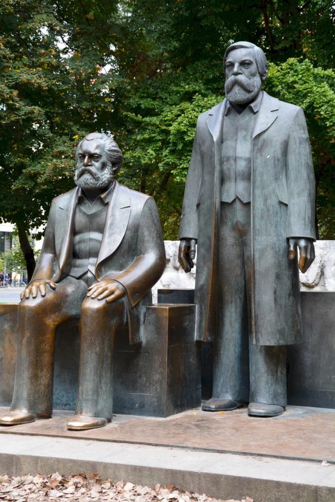 Bronzeskulpturen von zwei historischen Figuren im Freien vor grünen Bäumen in einem Park.