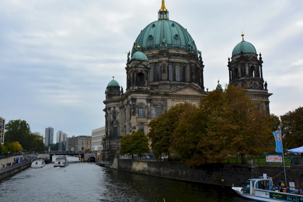 Berliner Dom am Flussufer mit Booten und herbstlicher Kulisse, ideale Sehenswürdigkeit in Berlin.