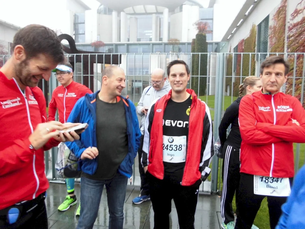 Gruppe von Männern in Sportkleidung vor einem Gebäude während einer Laufveranstaltung an einem bewölkten Tag.