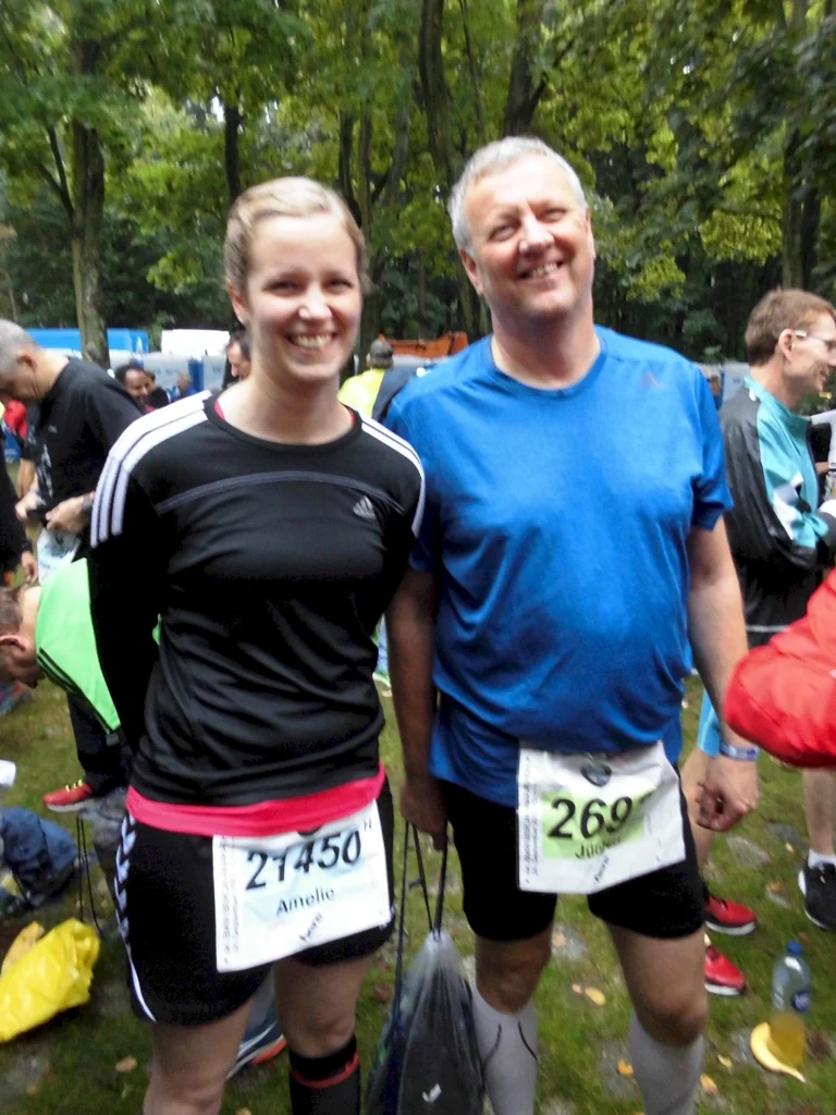 Zwei glückliche Menschen nach einem Laufwettbewerb im Park, mit Startnummern und sportlicher Ausrüstung.