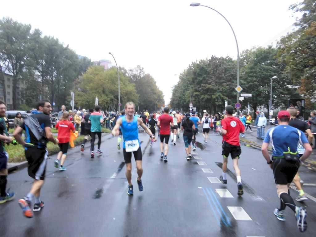 Läufer beim Marathon auf nasser Straße, umgeben von Bäumen und Zuschauern. Dynamische Sportveranstaltung im Freien.