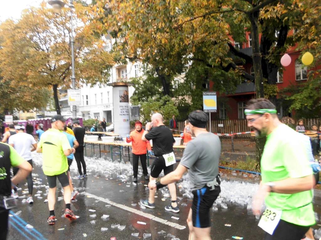 Läufer an Verpflegungsstation eines Stadtmarathons mit Herbstbäumen im Hintergrund. Plastikbecher auf dem Boden.
