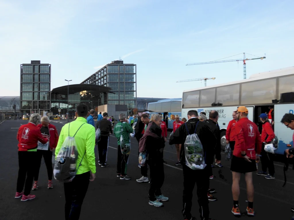 Gruppe von Läufern versammelt sich vor einem modernen Gebäude, Bus im Hintergrund, Vorbereitung auf ein Event.