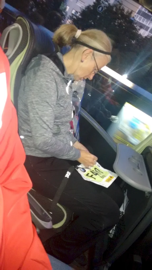 Person mit Pferdeschwanz sitzt in einem Bus und betrachtet eine Startnummer. Sie trägt sportliche Kleidung.