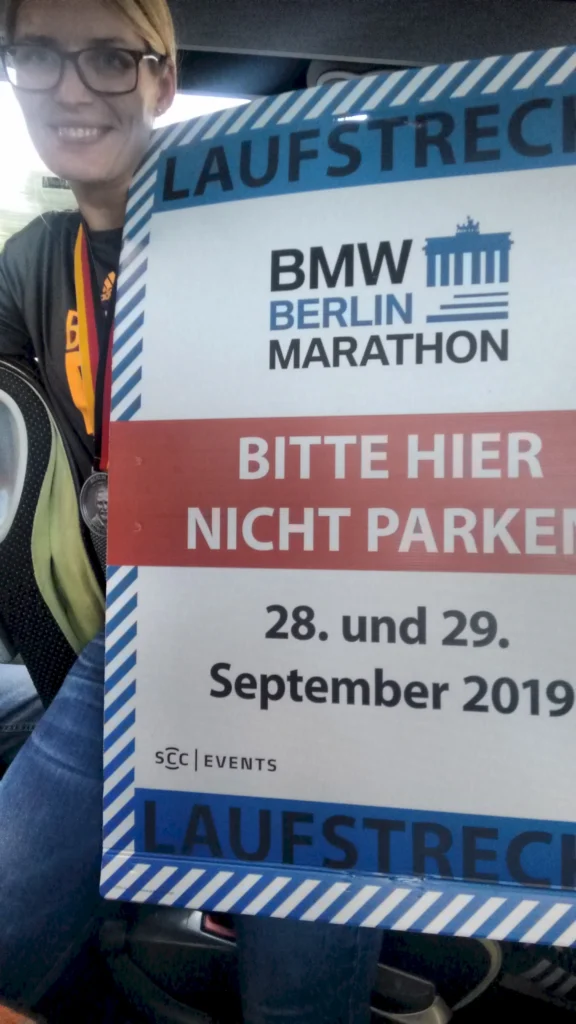 Frau mit Brille hält ein Schild für den BMW Berlin Marathon 2019 mit Hinweis Bitte hier nicht parken.