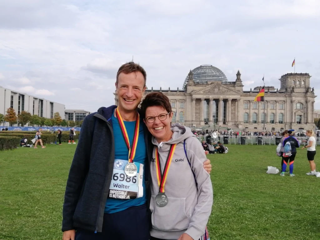 Zwei glückliche Marathonläufer mit Medaillen vor dem Berliner Reichstagsgebäude.