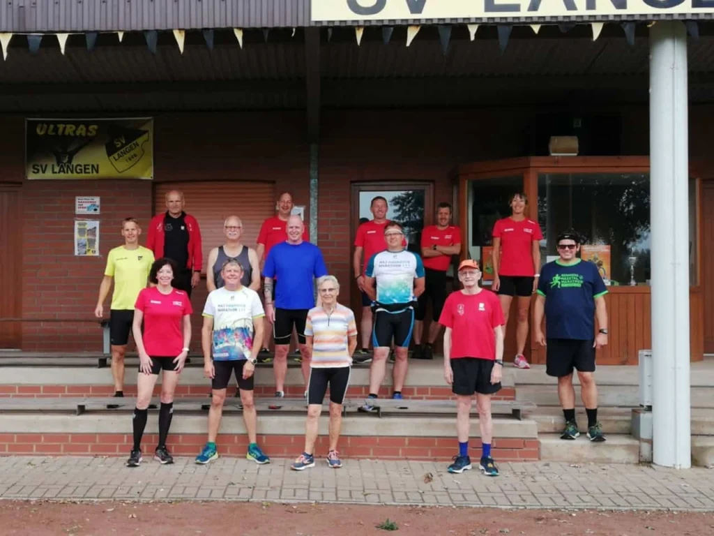 Gruppe von Läufern in Sportkleidung vor dem Vereinsgebäude des SV Langen, das Banner "ULTRAS SV LANGEN" sichtbar. Die Teilnehmer stehen auf den Stufen und posieren für ein Gruppenfoto.
