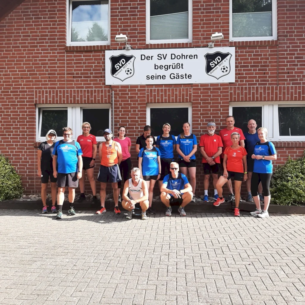 Gruppenfoto von Mitgliedern des SV Dohren vor dem Vereinsgebäude, die Besucher willkommen heißen. Die Sportler tragen verschiedene Trikots in Blau und Rot und stehen auf dem Gehweg.